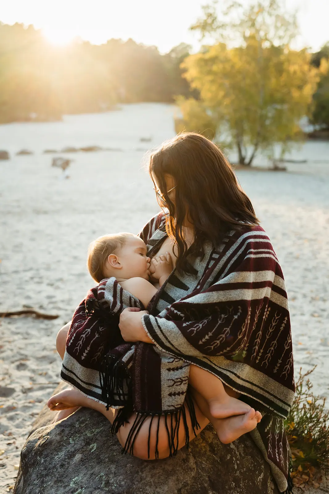 Photo colorée au coucher du soleil d'une maman qui allaite son bébé dans un moment de peau à peau pendant une séance photo allaitement dans la forêt de Fontainebleau