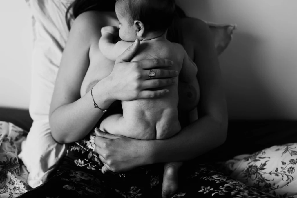 Photo noir et blanc d'une maman en peau à peau avec son bébé pendant une séance photo de naissance à domicile