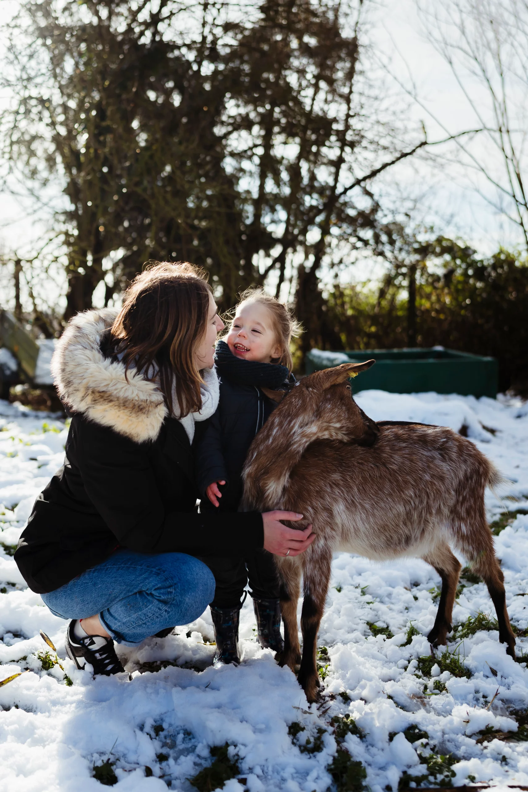 Portrait d'une maman et de son fil qui caressent leur chèvre dans leur jardin pendant une séance photo de famille avec animaux à fontainebleau