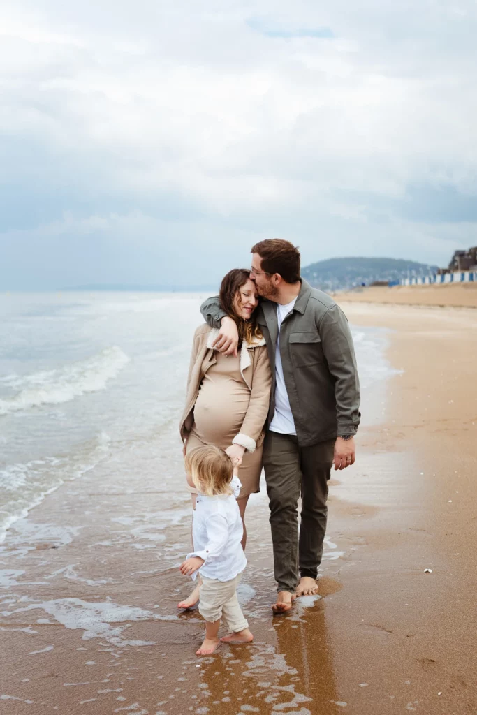 Couple de futurs parents complices marchant sur la plage pendant une séance photo grossesse.