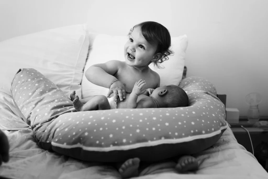Photo d'une grande soeur portant sa petite soeur pendant une séance photo de naissance à domicile