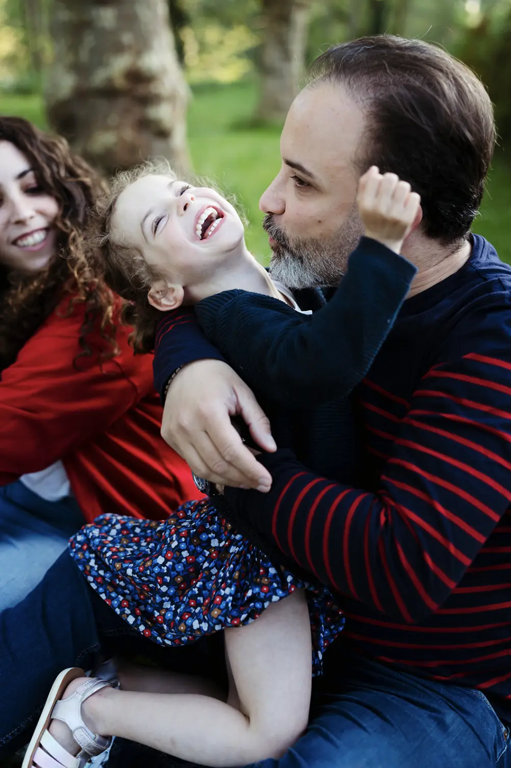 Portrait coloré et naturelle d'une petite fille riant aux éclats avec son papa pendant une séance photo de famille à fontainebleau