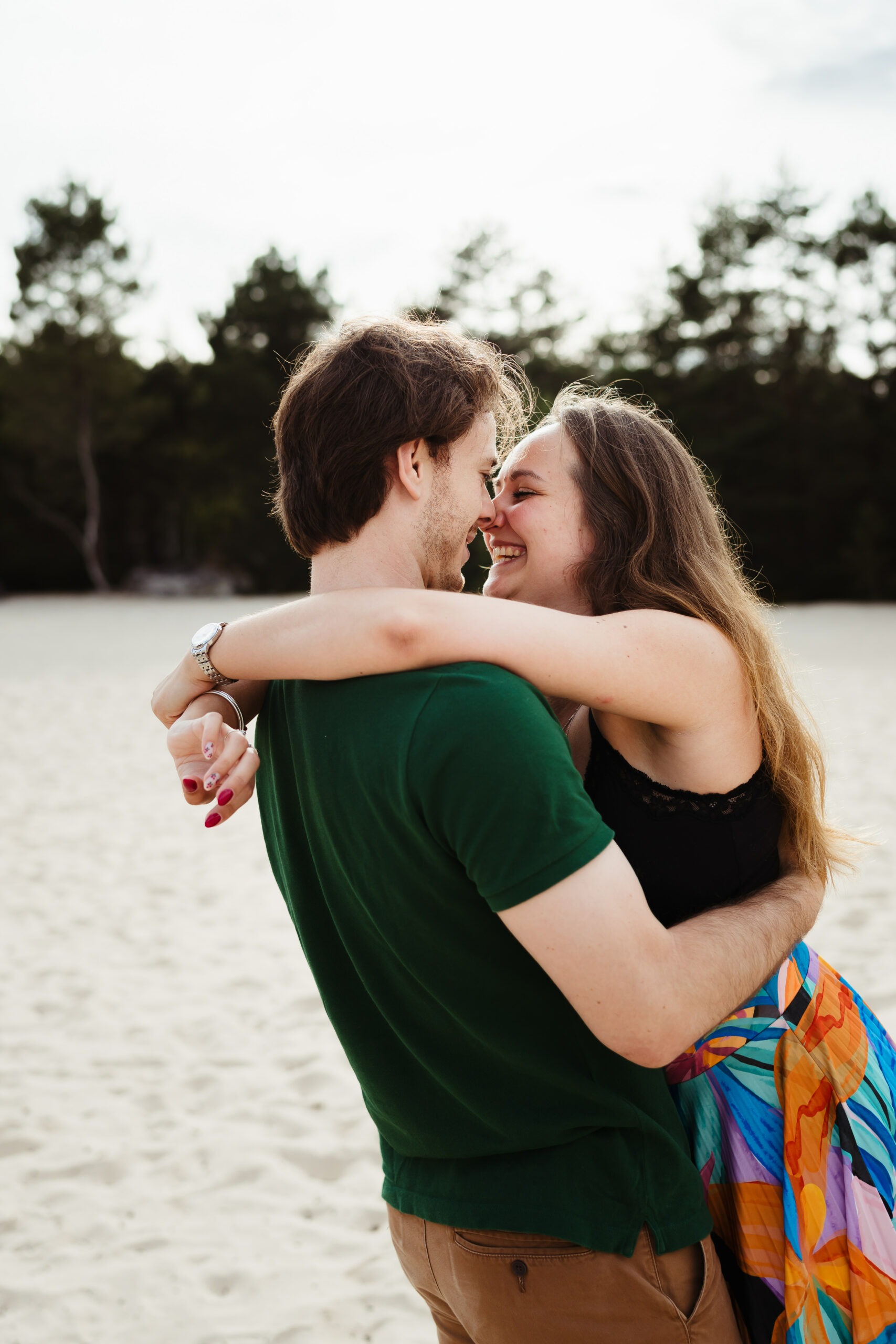 Deux amoureux s'embrassant en riant sur le sable pendant une séance photo dans la forêt de Fontainebleau